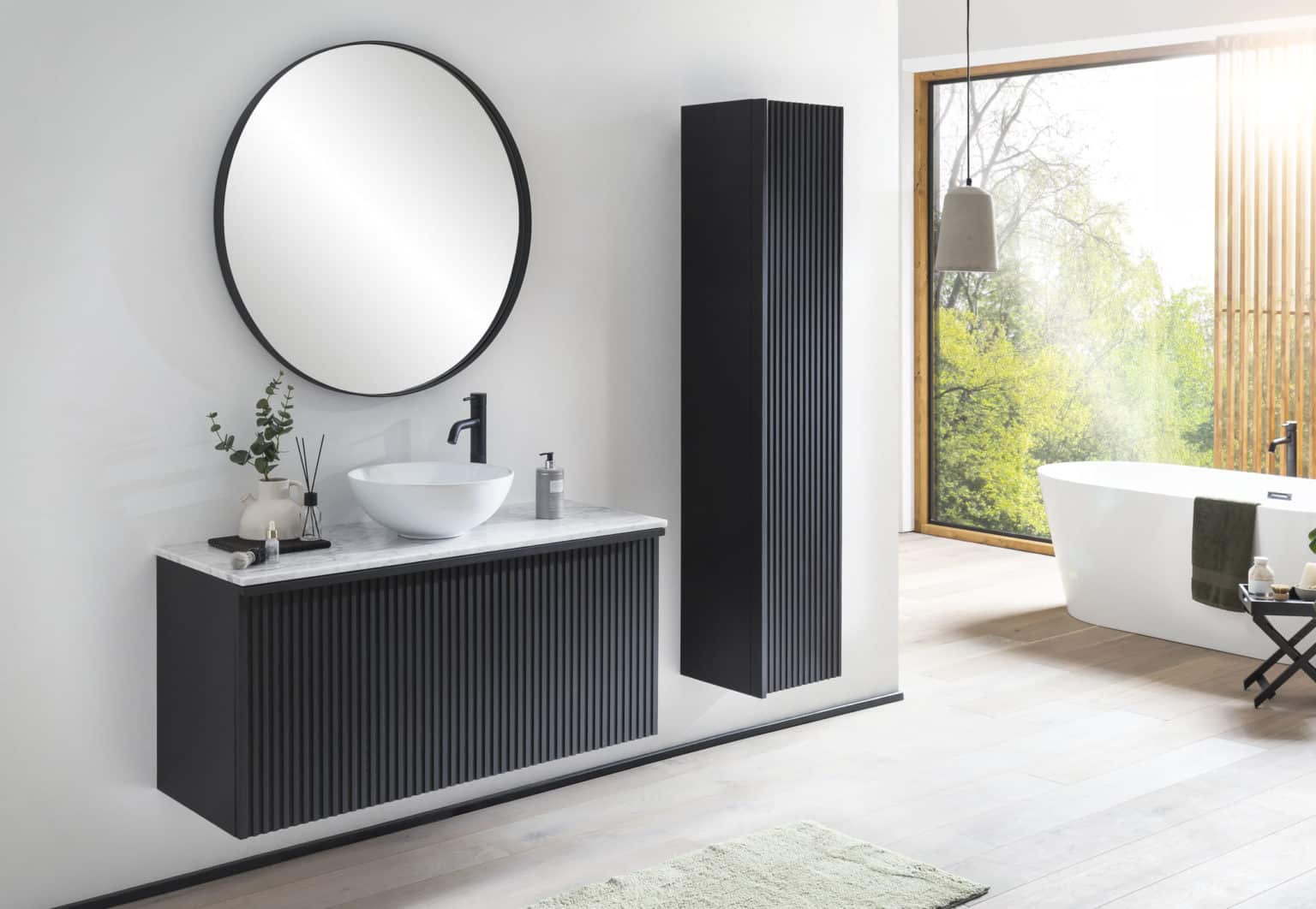 Een hangend badkamermeubel van massief hout in zwart met houten latjes aan de voorkant. Met boven het meubel een zwarte spiegel en rechtst naast het badkamermeubel met latjes een kolomkast