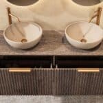 Rond donker eiken wastafelmeubel 140 cm met groevenfront en twee handgemaakte beige limestone waskommen