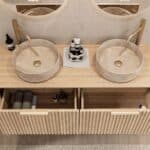 Rond hangend naturel eiken wastafelmeubel 140 cm met groevenfront en twee beige marmerlook waskommen