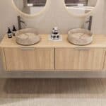 Rond hangend naturel eiken wastafelmeubel 160 cm met afgeronde hoeken en twee beige marmerlook waskommen