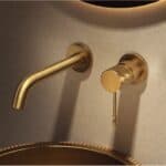 Moderne muurwastafelkraan in geborsteld goud voor wandmontage boven een wastafel of waskom, geleverd als complete set inclusief bijpassende clickwaste met duurzame PVD-coating. De clickwaste is een handige pop-up afvoer die je eenvoudig opent en slui