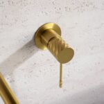 Moderne muurwastafelkraan in geborsteld goud voor wandmontage boven een wastafel of waskom. Voorzien van een duurzame PVD-coating, 5 jaar garantie en verkrijgbaar in 6 kleuren. Kenmerkend voor de Toscana serie is het gedraaide reliëf op de bediening:
