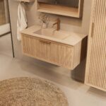 Het Riva badkamermeubel 100 in naturel eiken combineert ambachtelijk vakmanschap met moderne luxe. Gemaakt van massief eiken met ribbelfront, softclose lades en een mat beige Mineraalsteen wastafel. De wastafel kan met of zonder kraangaten worden gel