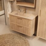 Het Riva badkamermeubel 100 in naturel eiken combineert ambachtelijk vakmanschap met moderne luxe. Gemaakt van massief eiken met ribbelfront, twee softclose lades en een mat beige Mineraalsteen wastafel. De wastafel kan met of zonder kraangaten worde