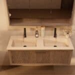 Het Riva badkamermeubel 120 in donker eiken ademt luxe en rust. Massief eiken met groevenfront, hoogwaardige softclose lades en een mat beige Mineraalsteen dubbel wastafel. De wastafel kan met of zonder kraangaten worden geleverd.