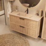 Het Riva badkamermeubel 120 in naturel eiken combineert ambachtelijk vakmanschap met moderne luxe. Gemaakt van massief eiken met ribbelfront, twee softclose lades en een mat beige Mineraalsteen wastafel. De wastafel kan met of zonder kraangaten worde
