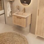 Het Riva badkamermeubel 60 in naturel eiken combineert ambachtelijk vakmanschap met moderne luxe. Gemaakt van massief eiken met ribbelfront, softclose lades en een mat beige Mineraalsteen wastafel. De wastafel kan met of zonder kraangaten worden gele