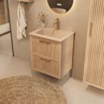 Het Riva badkamermeubel 60 in naturel eiken combineert ambachtelijk vakmanschap met moderne luxe. Gemaakt van massief eiken met ribbelfront, twee softclose lades en een mat beige Mineraalsteen wastafel. De wastafel kan met of zonder kraangaten worden