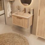 Het Riva badkamermeubel 70 in naturel eiken combineert ambachtelijk vakmanschap met moderne luxe. Gemaakt van massief eiken met ribbelfront, softclose lades en een mat beige Mineraalsteen wastafel. De wastafel kan met of zonder kraangaten worden gele