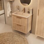 Het Riva badkamermeubel 70 in naturel eiken combineert ambachtelijk vakmanschap met moderne luxe. Gemaakt van massief eiken met ribbelfront, twee softclose lades en een mat beige Mineraalsteen wastafel. De wastafel kan met of zonder kraangaten worden