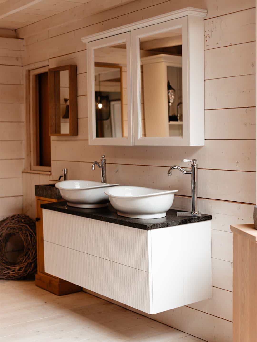 Wit meubel met twee waskommen en een spiegelkast tegen een houten wand